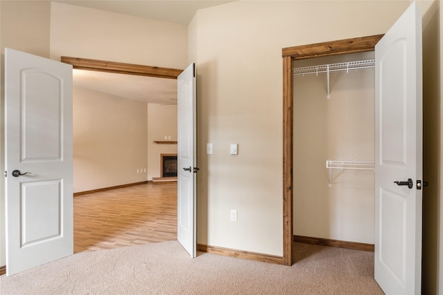 unfurnished bedroom with a closet, carpet flooring, baseboards, and a fireplace with raised hearth