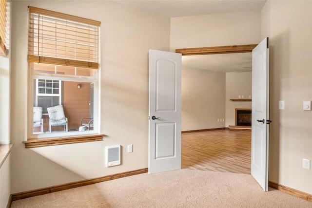 carpeted empty room with baseboards, a fireplace with raised hearth, and visible vents