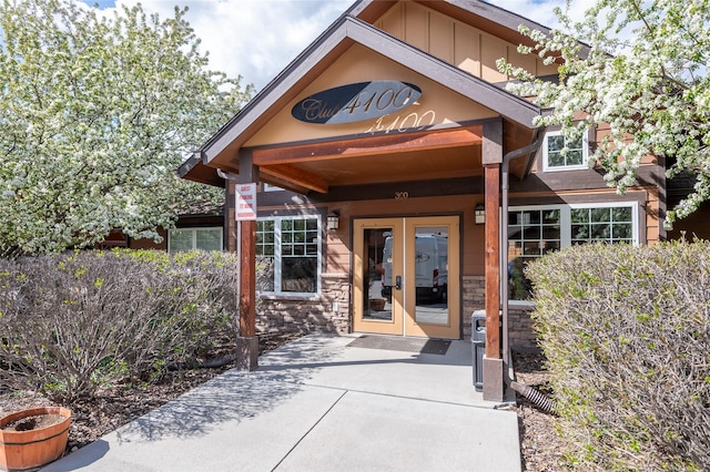 view of exterior entry with board and batten siding, french doors, and stone siding
