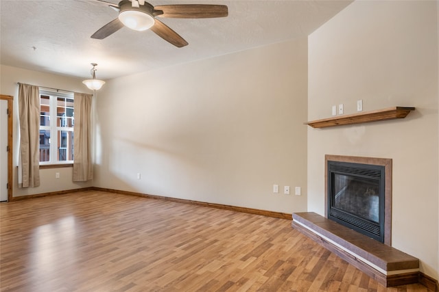 unfurnished living room with a glass covered fireplace, wood finished floors, baseboards, ceiling fan, and a textured ceiling