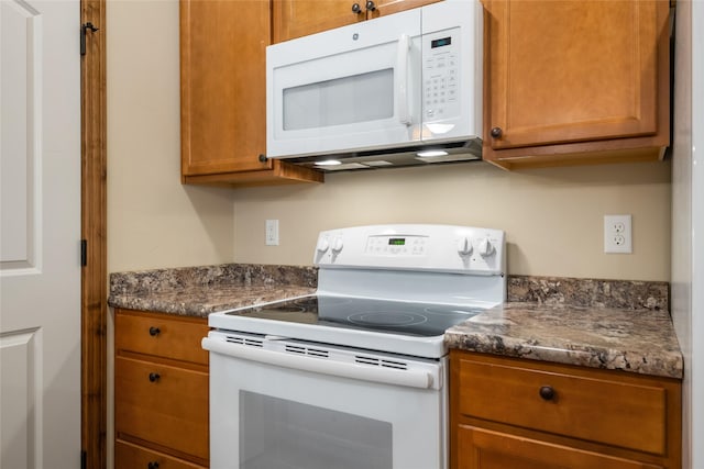 kitchen featuring dark countertops, brown cabinets, and white appliances