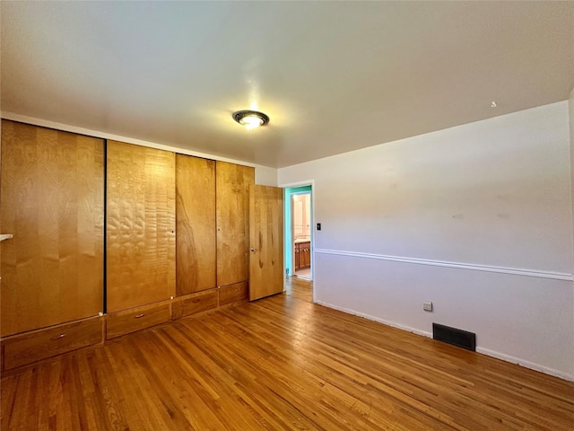 unfurnished bedroom featuring baseboards, a closet, wood finished floors, and visible vents