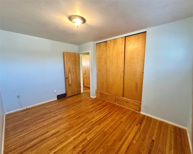 unfurnished bedroom featuring baseboards, wood finished floors, and a closet