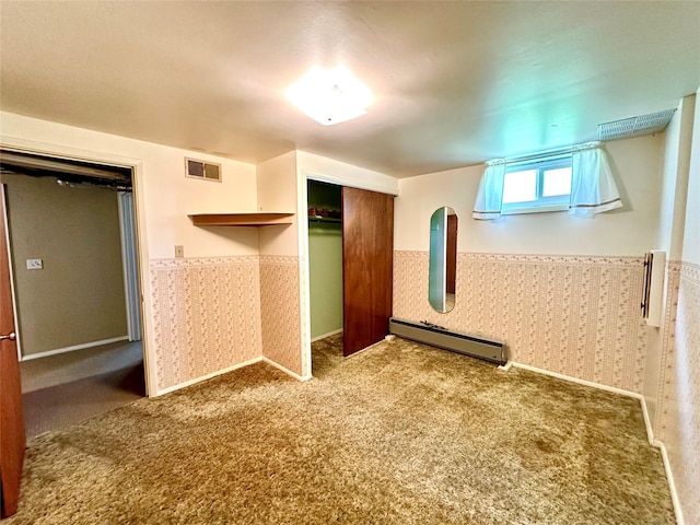 unfurnished bedroom with visible vents, a closet, wainscoting, baseboard heating, and carpet
