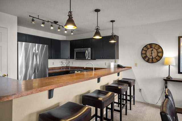kitchen with dark cabinets, appliances with stainless steel finishes, light carpet, and a kitchen breakfast bar