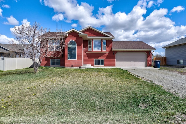 raised ranch with fence, a front yard, a shingled roof, an attached garage, and driveway