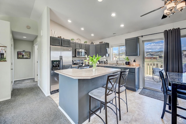 kitchen featuring ceiling fan, a breakfast bar, light countertops, stainless steel appliances, and vaulted ceiling