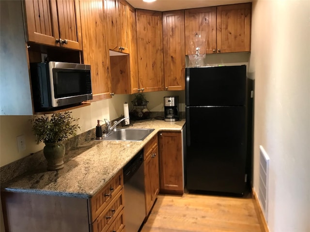 248 Forest Edge Trl, Kalispell, MT 59901 - kitchen with appliances with stainless steel finishes, a sink, light wood-type flooring, brown cabinetry, and stone countertops