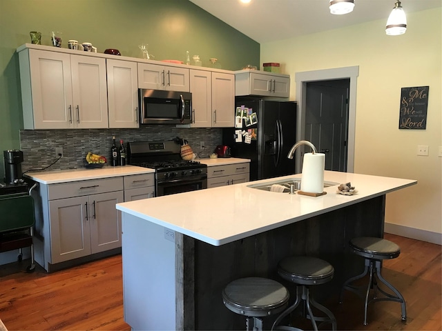 kitchen with black fridge, a sink, stainless steel microwave, gray cabinetry, and gas range oven