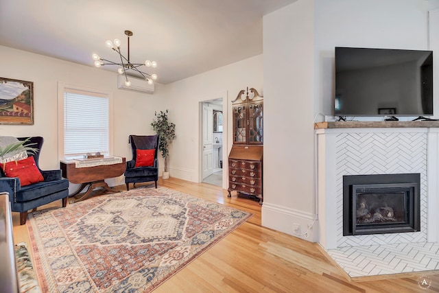 living area with wood finished floors, baseboards, a wall mounted air conditioner, a chandelier, and a tile fireplace