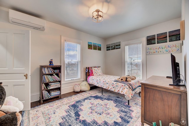 bedroom featuring wood finished floors, baseboards, and a wall unit AC