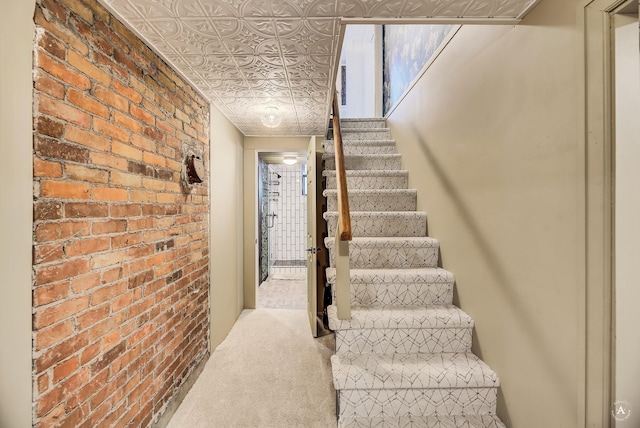 stairway featuring carpet flooring, an ornate ceiling, and brick wall