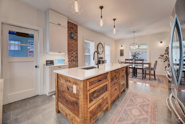 kitchen with pendant lighting, a kitchen island with sink, light countertops, white cabinets, and a sink