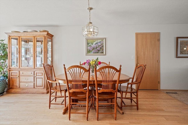 dining space with a textured ceiling, light wood-style flooring, and a notable chandelier
