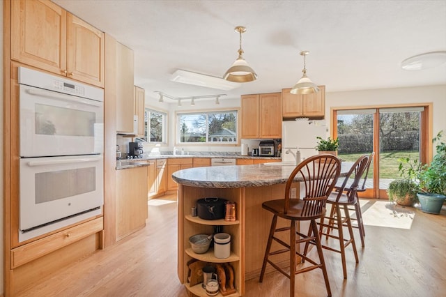 kitchen featuring white appliances, light brown cabinetry, a center island, and light wood-type flooring