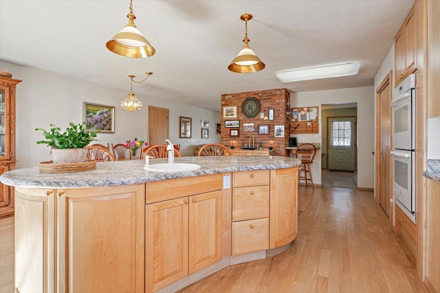 kitchen with light brown cabinets, double oven, light wood-type flooring, a sink, and hanging light fixtures