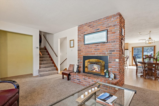 living room featuring carpet floors, a textured ceiling, stairs, and a brick fireplace