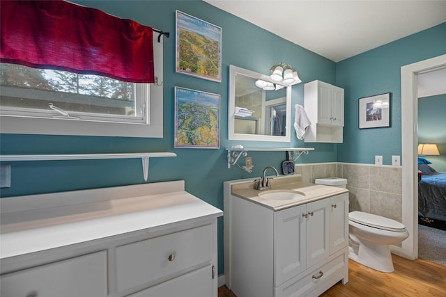 bathroom with vanity, wood finished floors, toilet, tile walls, and ensuite bathroom