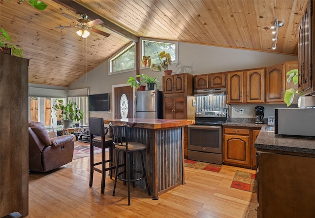 kitchen featuring brown cabinetry, a ceiling fan, dark countertops, high vaulted ceiling, and stainless steel appliances