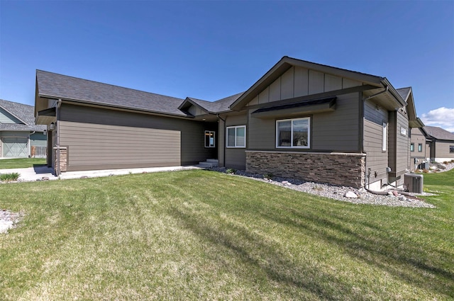 view of front facade featuring an attached garage, stone siding, board and batten siding, a front yard, and central air condition unit