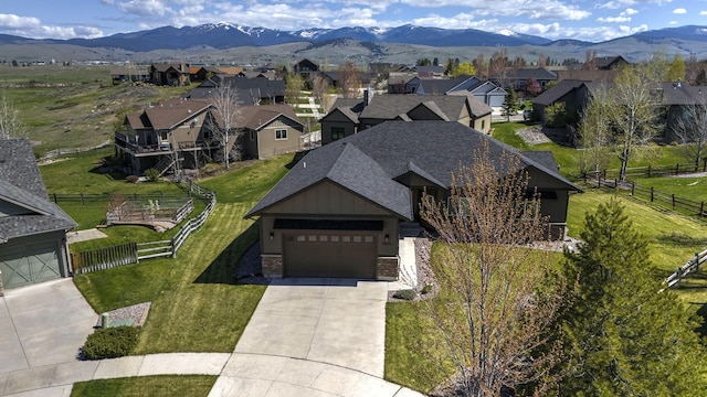 view of front facade with fence, a shingled roof, stone siding, a front yard, and driveway