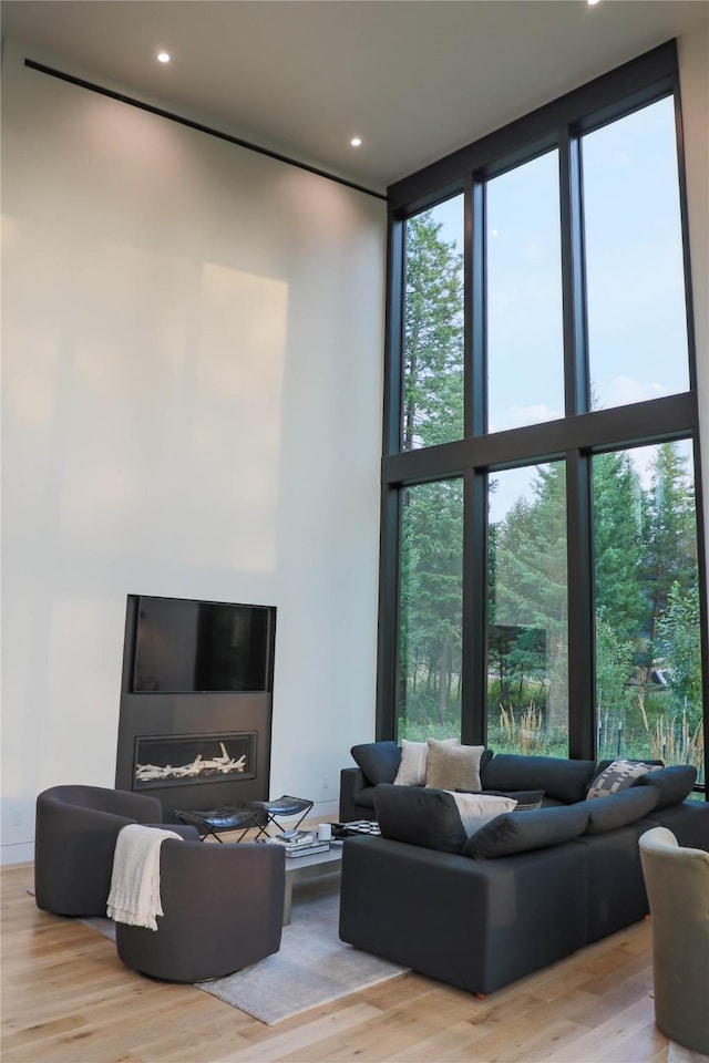 living area featuring a wall of windows, recessed lighting, wood finished floors, and a towering ceiling