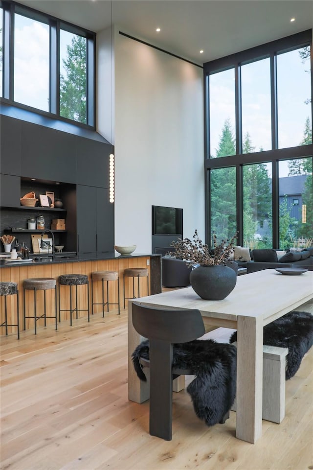 dining space with a towering ceiling, recessed lighting, a wall of windows, and light wood-type flooring