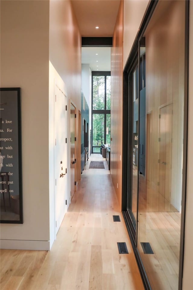 corridor with expansive windows, light wood finished floors, a towering ceiling, and visible vents