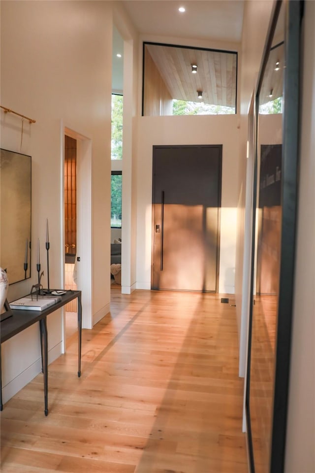 hall with recessed lighting, light wood-type flooring, elevator, and a towering ceiling