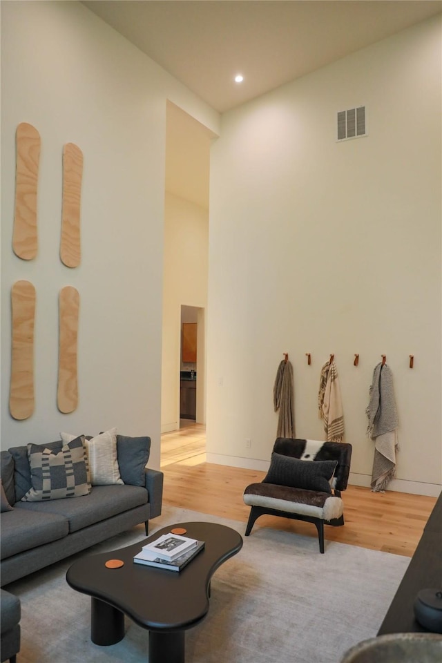 living area featuring a towering ceiling, visible vents, wood finished floors, baseboards, and recessed lighting