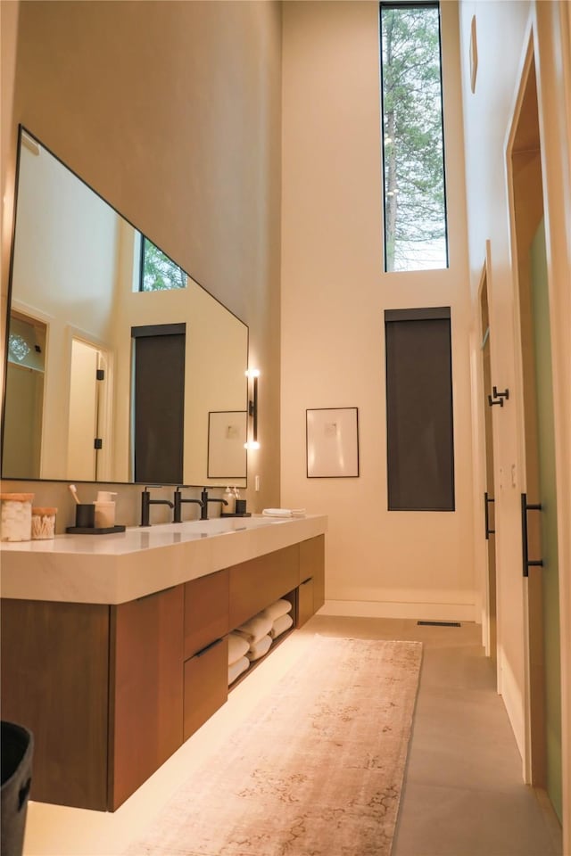 bathroom featuring double vanity, baseboards, a sink, and a towering ceiling