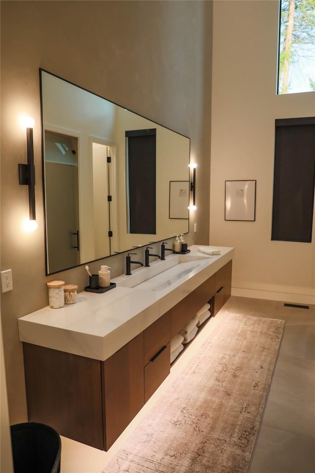 bathroom with a high ceiling, a sink, double vanity, baseboards, and visible vents