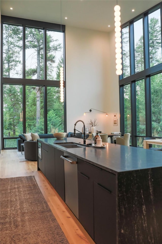 kitchen with floor to ceiling windows, pendant lighting, a sink, light wood finished floors, and dark stone counters