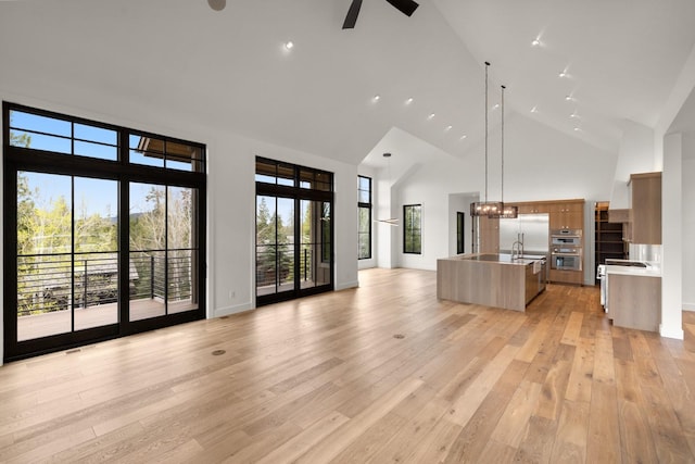 unfurnished living room featuring a sink, light wood-style floors, high vaulted ceiling, ceiling fan with notable chandelier, and baseboards