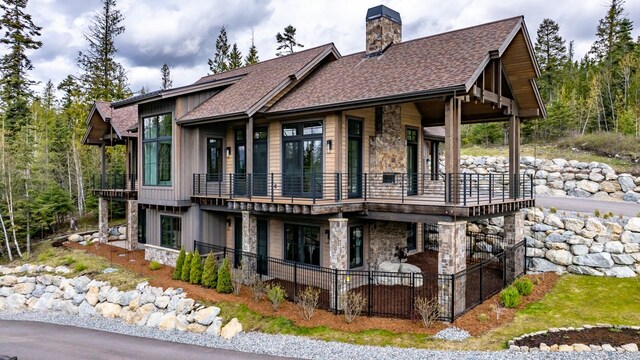back of house with a shingled roof, a patio, a chimney, and stone siding