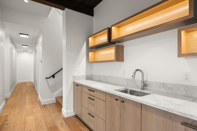 kitchen with a sink, light brown cabinets, light wood finished floors, and light stone counters