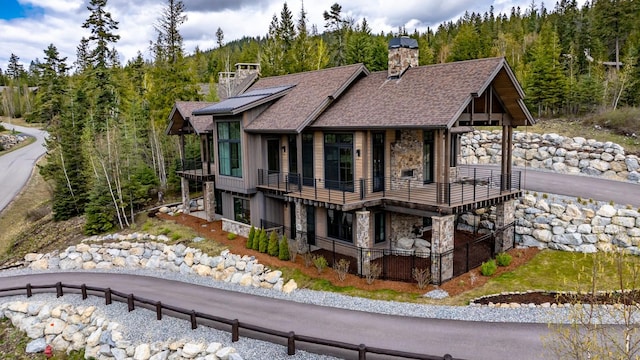 view of home's exterior featuring a balcony, stone siding, a chimney, a shingled roof, and a wooded view