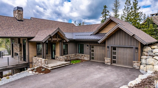 chalet / cabin with roof with shingles, a standing seam roof, stone siding, and aphalt driveway
