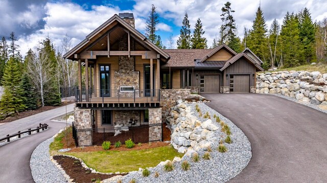 craftsman-style home with aphalt driveway, a garage, stone siding, a chimney, and a balcony