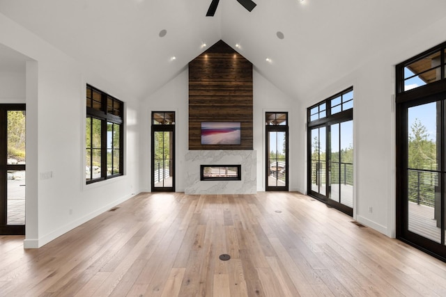 unfurnished living room with high vaulted ceiling, a healthy amount of sunlight, ceiling fan, and a high end fireplace