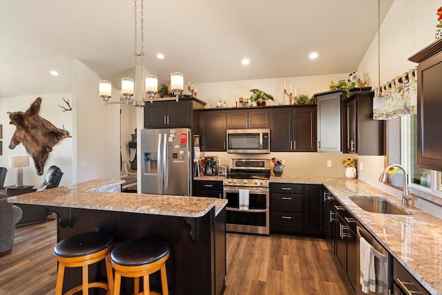 kitchen with appliances with stainless steel finishes, dark wood-style floors, a sink, and light stone counters