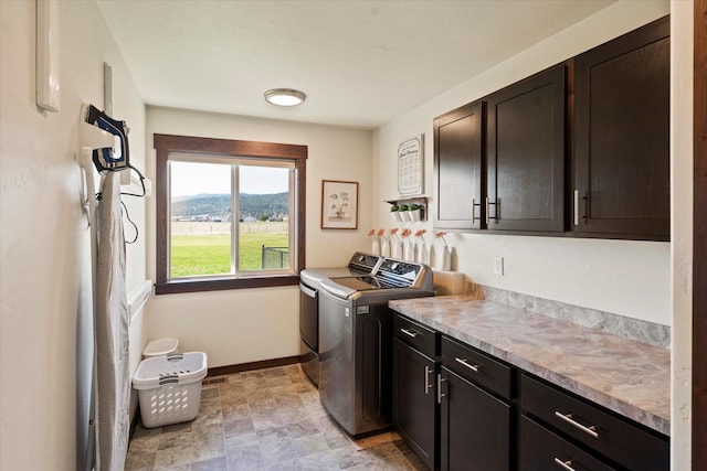 laundry room featuring baseboards, stone finish floor, a mountain view, washing machine and clothes dryer, and cabinet space