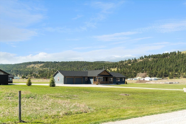 view of front facade featuring a garage, concrete driveway, a front lawn, and a forest view