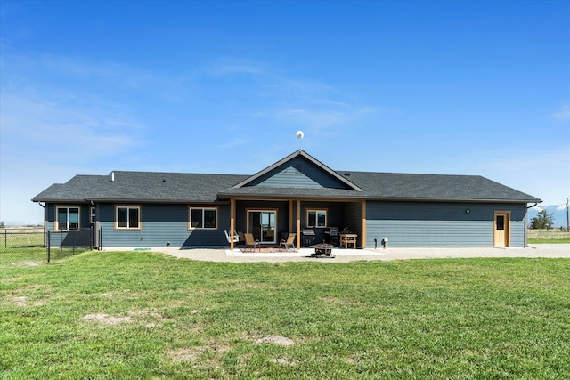 back of house featuring fence, roof with shingles, an outdoor fire pit, a lawn, and a patio