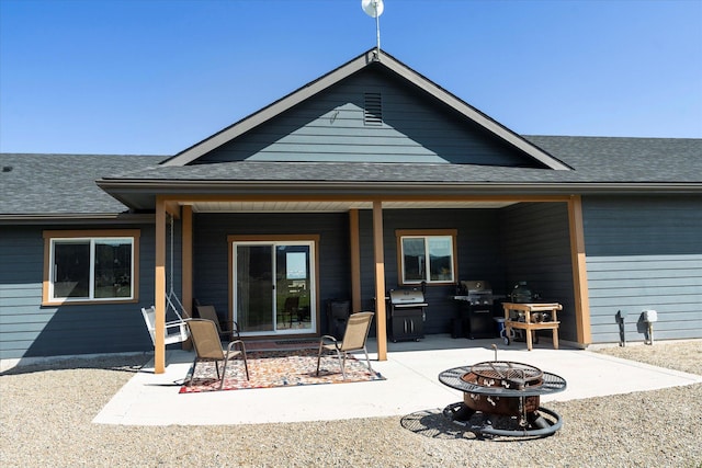 rear view of property with a patio, a shingled roof, and a fire pit