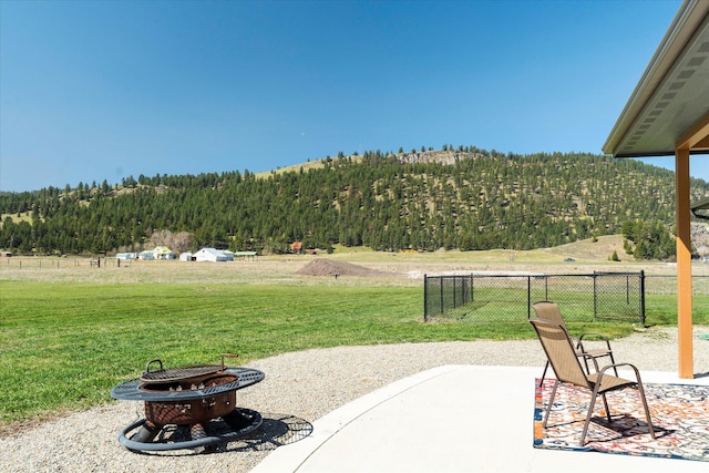 view of patio with a wooded view, fence, a fire pit, and a mountain view