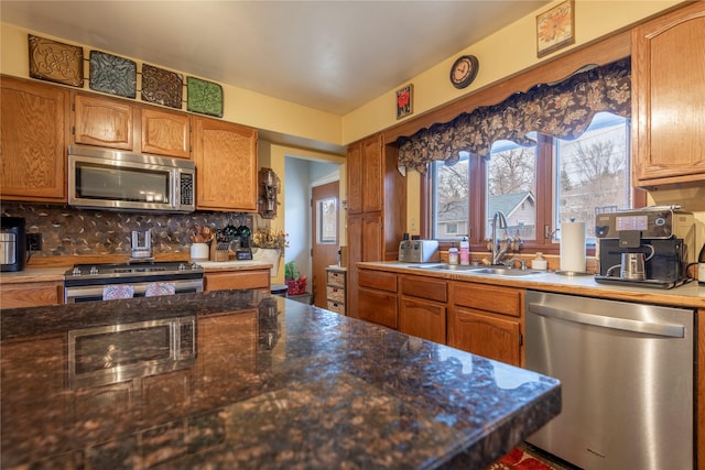 kitchen with appliances with stainless steel finishes, a sink, decorative backsplash, and brown cabinets