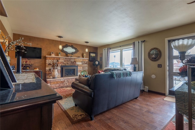 living room with wood finished floors, a stone fireplace, and baseboards