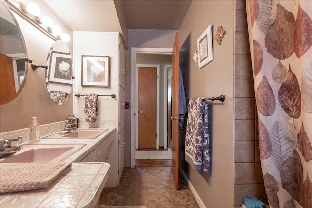 bathroom with stone finish flooring, baseboards, and double vanity