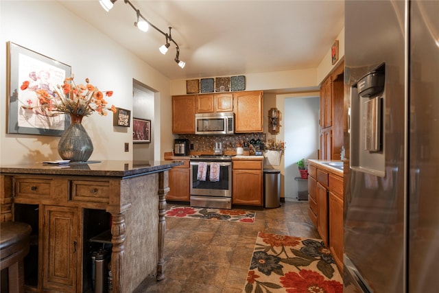 kitchen with stainless steel appliances, brown cabinetry, decorative backsplash, and dark stone finish flooring